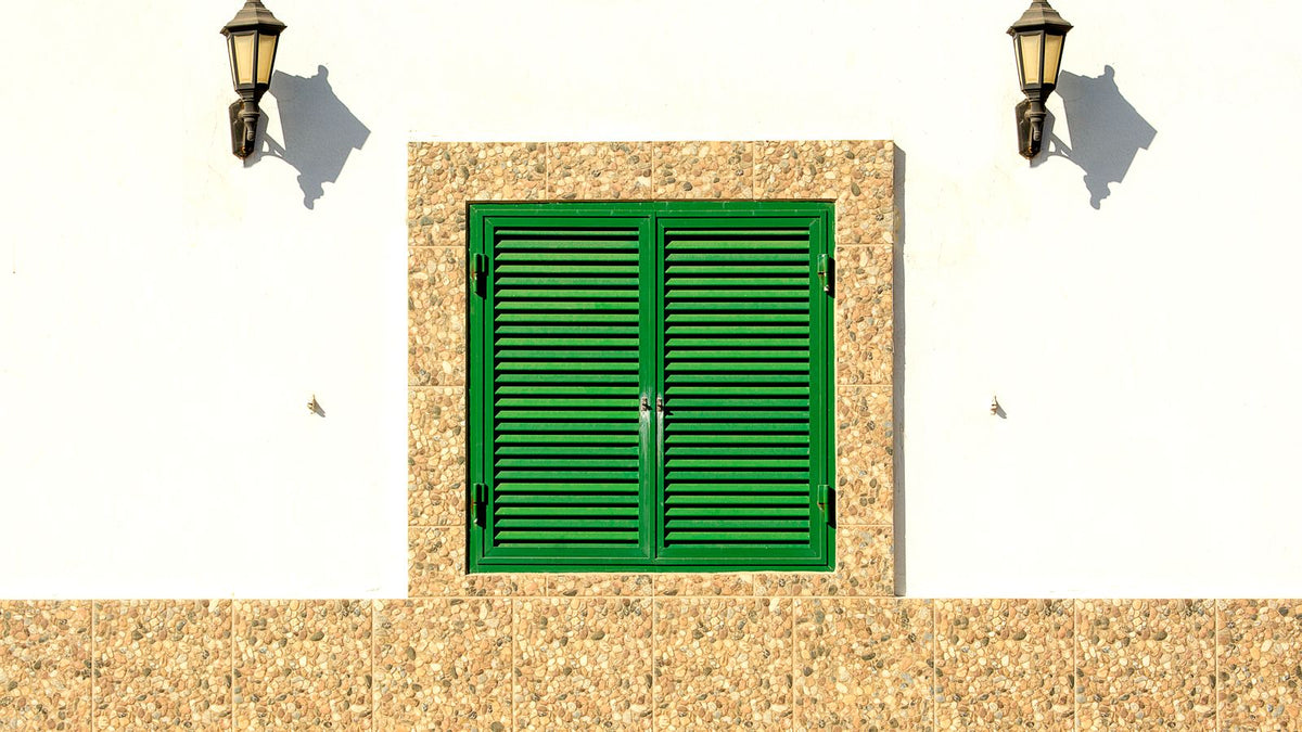 Deux appliques murales fixées de part et d'autre d'une fenêtre aux volets verts